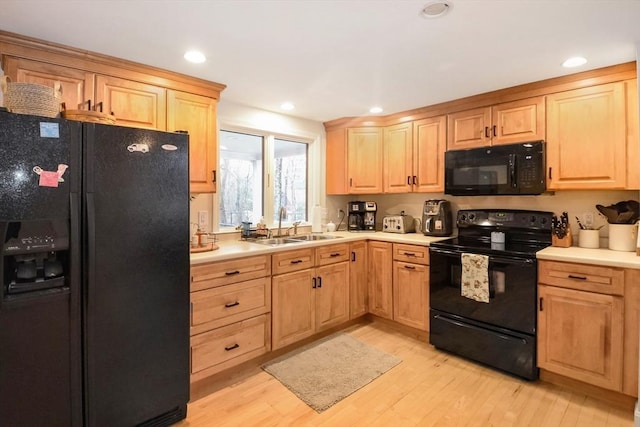 kitchen with light brown cabinets, light countertops, a sink, light wood finished floors, and black appliances