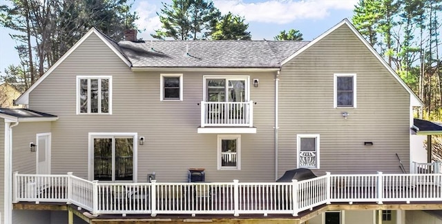 rear view of house featuring a deck, a chimney, and roof with shingles