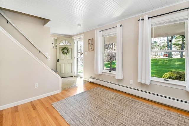 foyer entrance featuring a baseboard heating unit, a healthy amount of sunlight, stairway, and wood finished floors