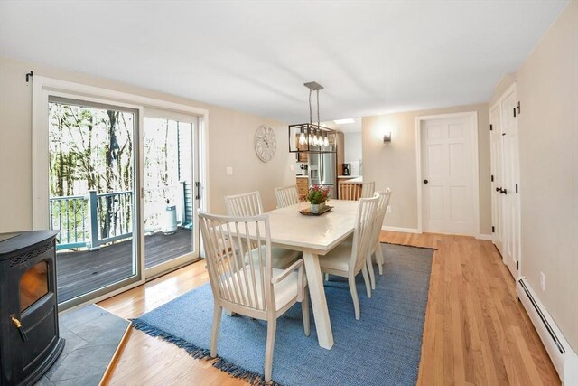 dining space featuring baseboard heating, a wood stove, baseboards, light wood finished floors, and a notable chandelier
