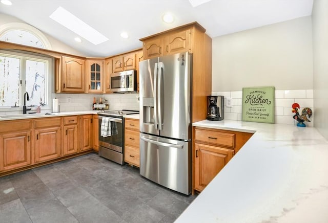 kitchen with backsplash, a sink, light countertops, lofted ceiling with skylight, and stainless steel appliances