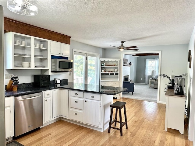 kitchen featuring stainless steel appliances, a peninsula, ceiling fan, white cabinetry, and light wood finished floors