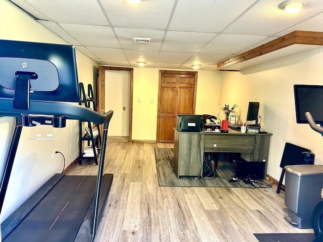 workout area featuring light wood finished floors, baseboards, and a drop ceiling