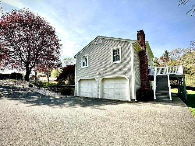 view of property exterior featuring a chimney, stairway, asphalt driveway, an attached garage, and a deck