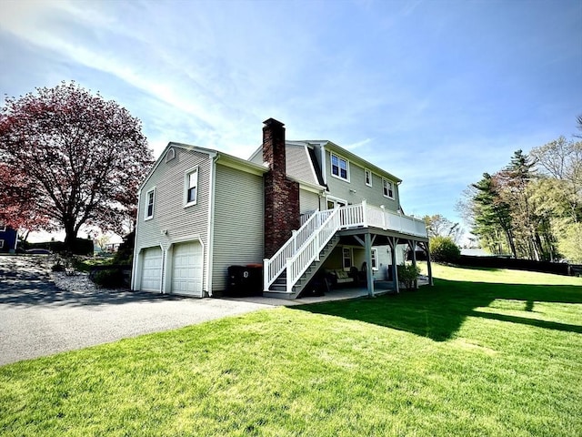 back of house with stairs, a garage, a chimney, driveway, and a yard