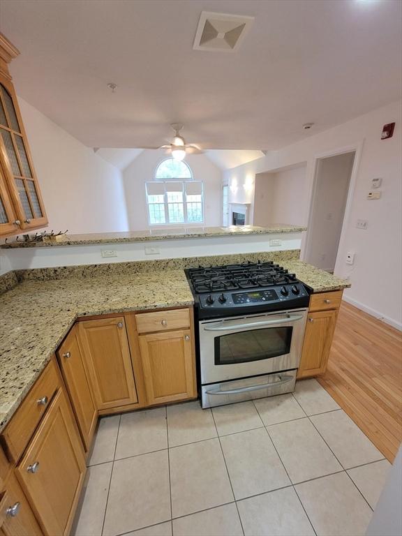 281 Rowley Bridge Rd Unit 7, Topsfield, MA 01983 - kitchen featuring stainless steel range with gas cooktop, ceiling fan, vaulted ceiling, light stone countertops, and glass insert cabinets
