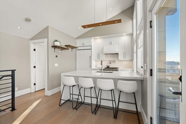 kitchen with extractor fan, paneled built in refrigerator, a peninsula, white cabinets, and a kitchen bar