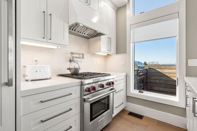 kitchen with light countertops, visible vents, white cabinets, luxury stove, and premium range hood