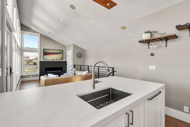 kitchen with a fireplace, white cabinetry, vaulted ceiling, a sink, and wood finished floors