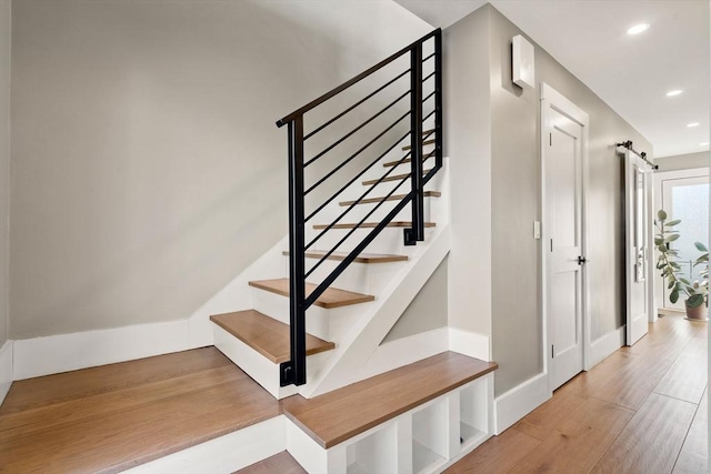 stairs with recessed lighting, a barn door, baseboards, and wood finished floors