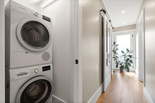 washroom with a barn door, laundry area, stacked washer / dryer, baseboards, and light wood finished floors