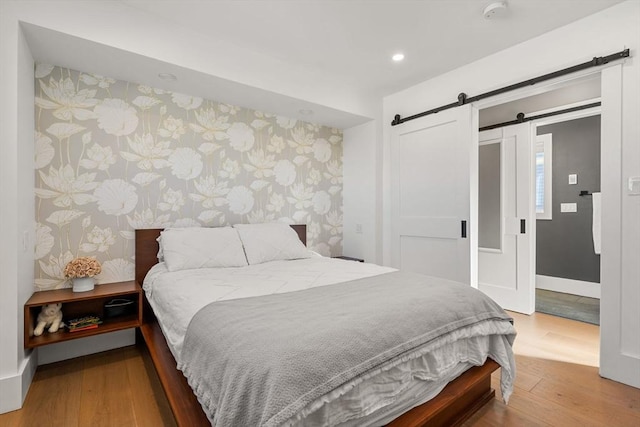 bedroom featuring recessed lighting, a barn door, wood finished floors, baseboards, and wallpapered walls