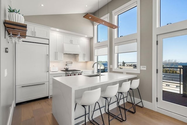 kitchen with high vaulted ceiling, built in fridge, exhaust hood, a sink, and light wood-type flooring