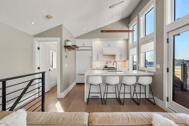 kitchen featuring white cabinets, a breakfast bar area, wood finished floors, a peninsula, and paneled refrigerator