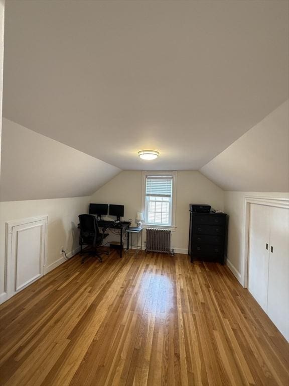 unfurnished office with radiator heating unit, vaulted ceiling, and light wood-type flooring