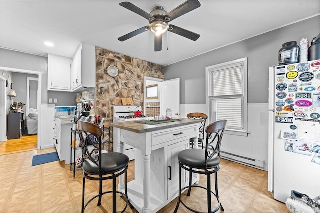 kitchen featuring white cabinetry, baseboard heating, a kitchen breakfast bar, white fridge, and stove