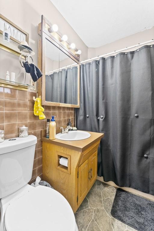 bathroom with a shower with curtain, vanity, toilet, and decorative backsplash