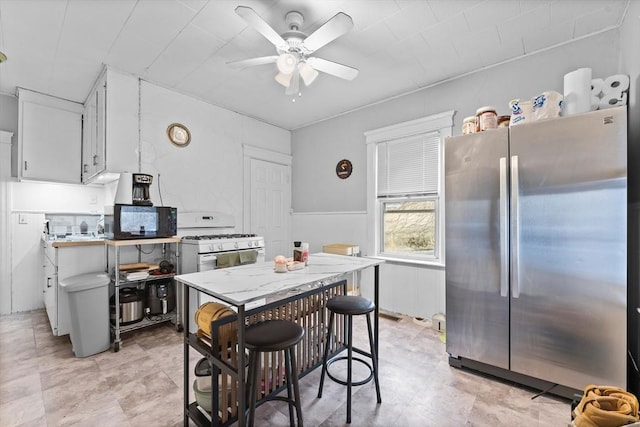 kitchen featuring stainless steel refrigerator, ceiling fan, white gas stove, and white cabinets