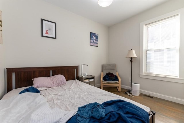 bedroom with multiple windows, wood finished floors, and baseboards