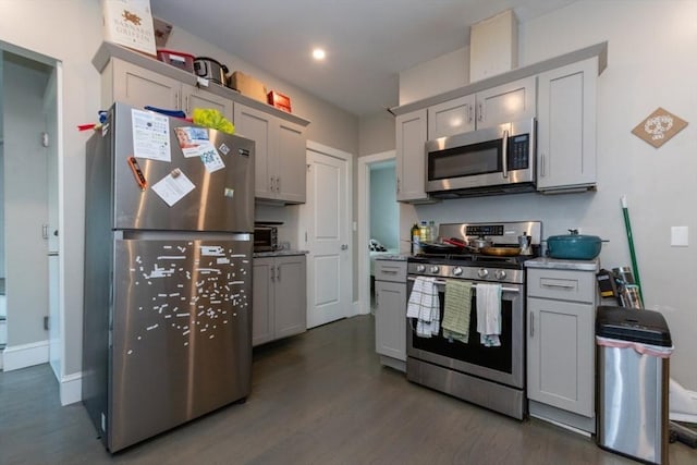 kitchen with stainless steel appliances, gray cabinetry, dark wood-type flooring, and baseboards