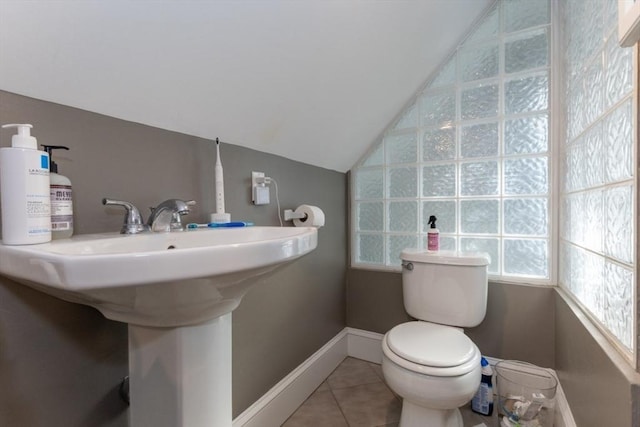 half bath with vaulted ceiling, tile patterned floors, toilet, baseboards, and a sink