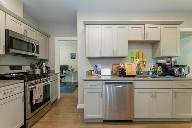 kitchen featuring appliances with stainless steel finishes, a sink, wood finished floors, a desk, and light countertops