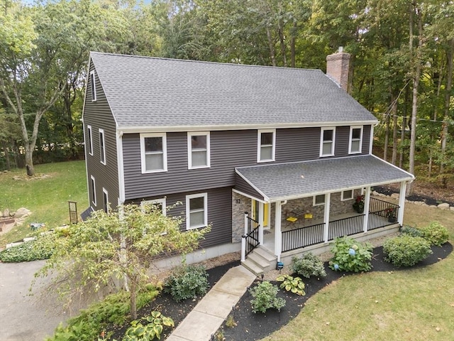 view of front of home featuring a front lawn, roof with shingles, covered porch, a chimney, and stone siding