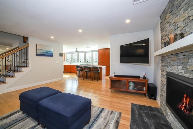 living room featuring a stone fireplace, baseboards, stairs, and light wood-style floors