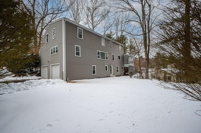 snow covered rear of property featuring a garage