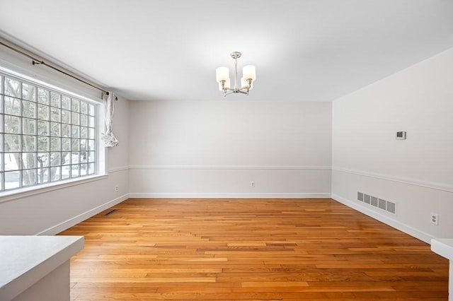 empty room featuring a notable chandelier and light hardwood / wood-style floors