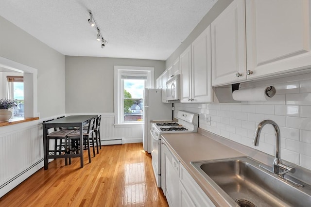 kitchen featuring white appliances, white cabinetry, a baseboard heating unit, a sink, and light wood finished floors