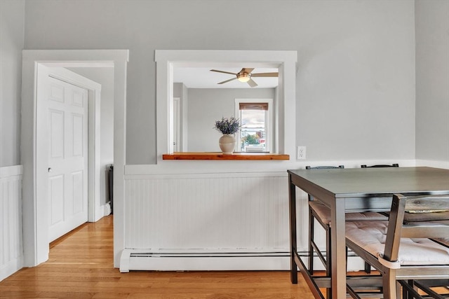 dining space with a ceiling fan, light wood finished floors, and a wainscoted wall