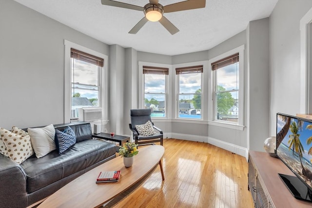 living area featuring baseboards, a ceiling fan, light wood-type flooring, and a wealth of natural light