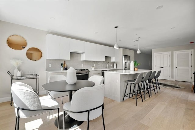 kitchen featuring decorative light fixtures, tasteful backsplash, a kitchen island, white cabinetry, and appliances with stainless steel finishes