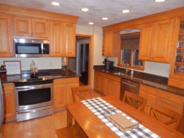 kitchen featuring a sink, dark stone counters, light wood-style floors, and appliances with stainless steel finishes