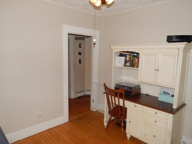 office area featuring light wood-style flooring, baseboards, baseboard heating, and built in desk