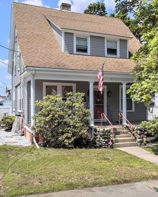 view of front of home with a porch, a front lawn, roof with shingles, and a chimney