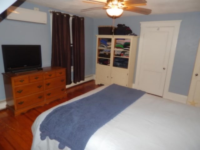 bedroom with baseboard heating, a wall mounted air conditioner, ceiling fan, and wood finished floors