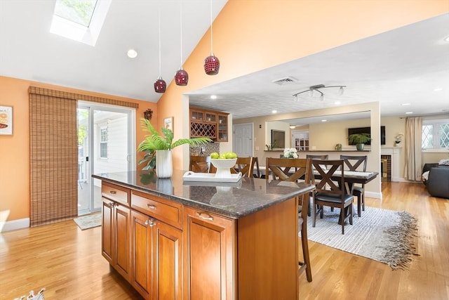 kitchen with light wood-style flooring, brown cabinets, a kitchen breakfast bar, open floor plan, and vaulted ceiling