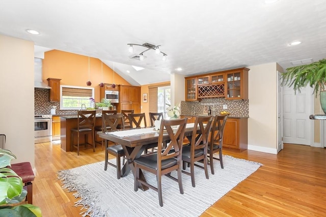 dining area featuring lofted ceiling, light wood-type flooring, recessed lighting, and bar