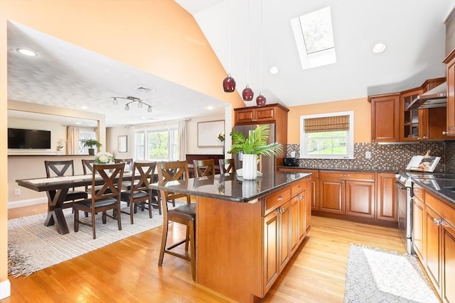 kitchen featuring stainless steel stove, a kitchen breakfast bar, light wood-style flooring, a skylight, and brown cabinets