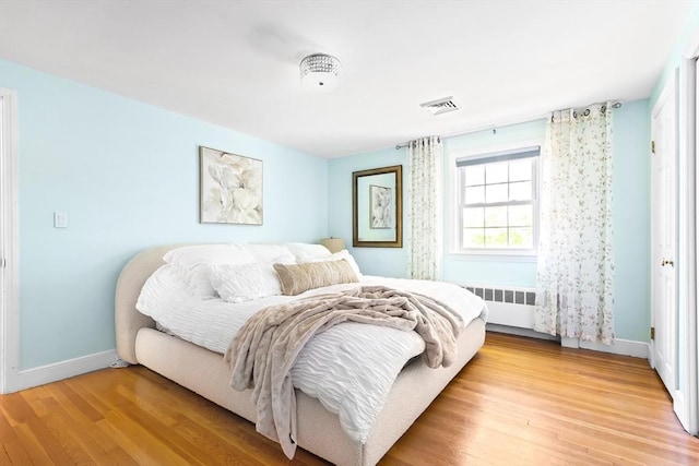 bedroom featuring radiator heating unit, light wood finished floors, and baseboards