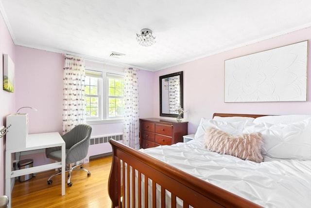bedroom featuring radiator heating unit, light wood-style flooring, ornamental molding, and a desk