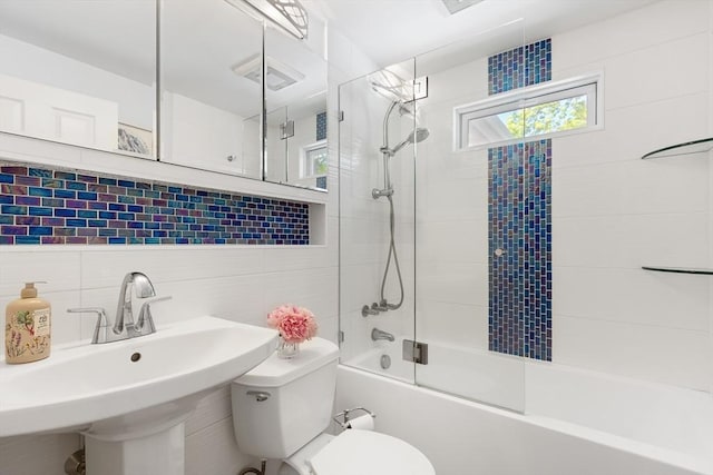 bathroom with a sink, toilet, bath / shower combo with glass door, and tile walls