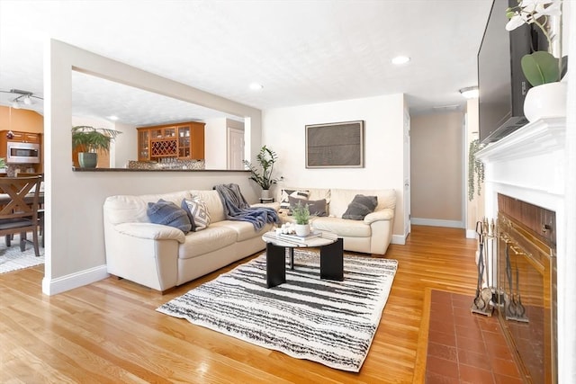 living room with baseboards, wood finished floors, a fireplace with flush hearth, and recessed lighting