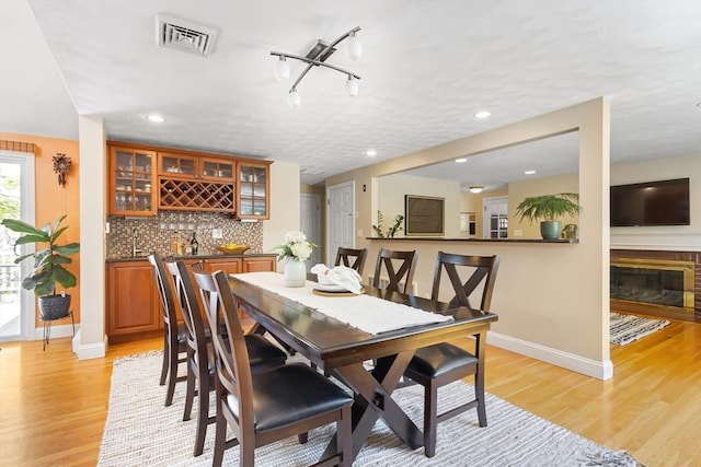 dining room featuring wet bar, baseboards, light wood-style floors, recessed lighting, and a glass covered fireplace