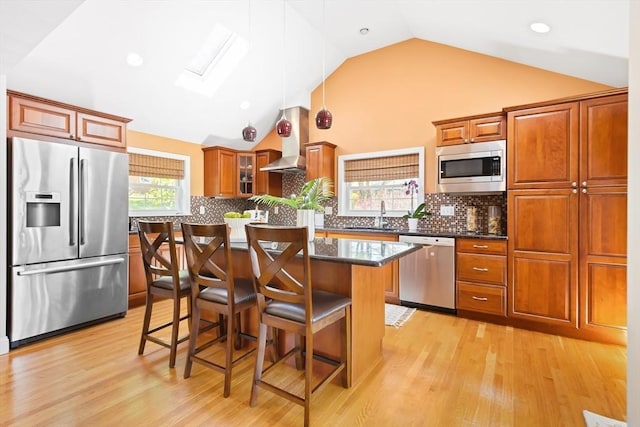 kitchen featuring appliances with stainless steel finishes, a skylight, a breakfast bar, brown cabinetry, and a center island