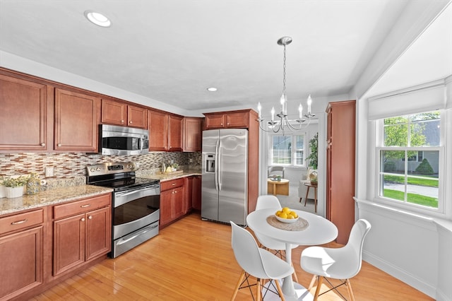 kitchen with stainless steel appliances, backsplash, a chandelier, light wood-style flooring, and light stone countertops