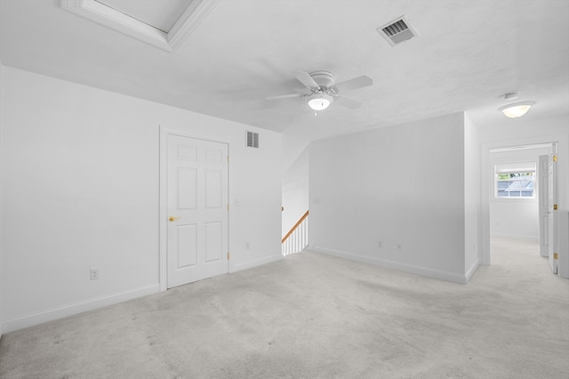 spare room featuring light colored carpet, a ceiling fan, and baseboards