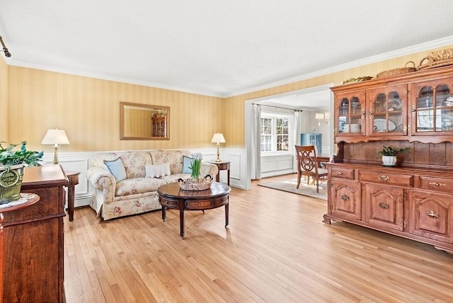 living room with light wood-style flooring, baseboard heating, crown molding, and wainscoting